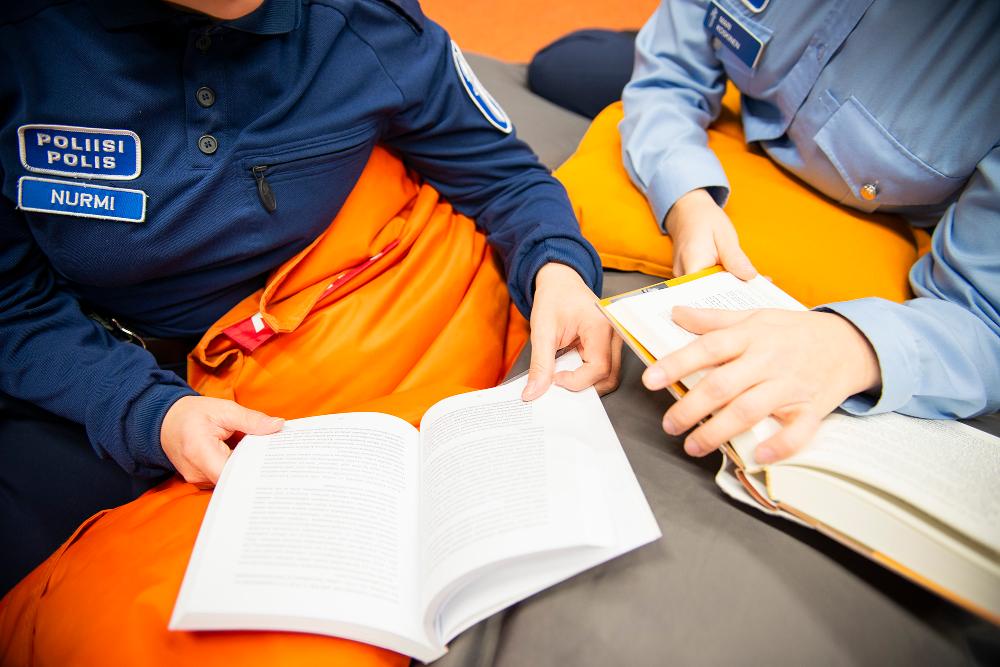 Two uniformed police students browsing books while sat on beanbags in the library.